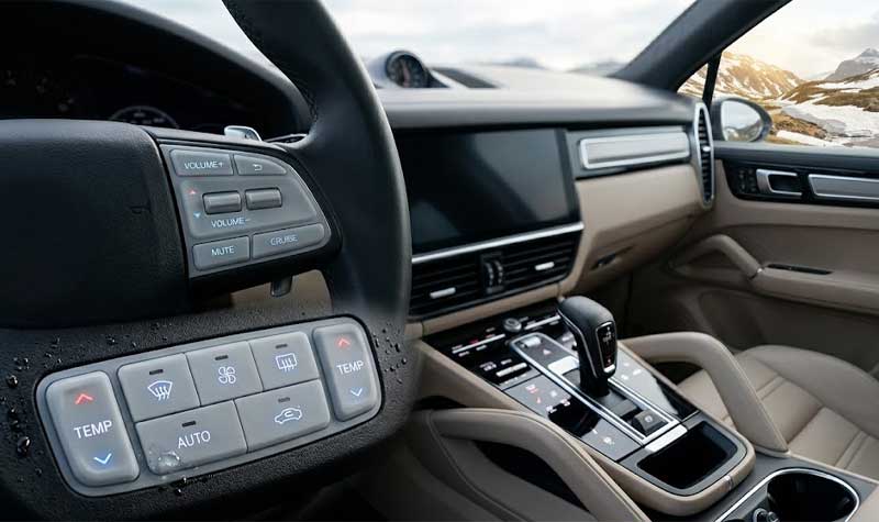 Close up of the steering wheel and center console controls of a modern luxury car like a Porsche Cayenne with a scenic mountain pass view through the windscreen