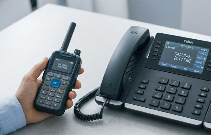A person holds a rugged walkie talkie next to a multi line office desk phone on a clean surface showcasing the durable Telecommunication Devices Silicone Keypads