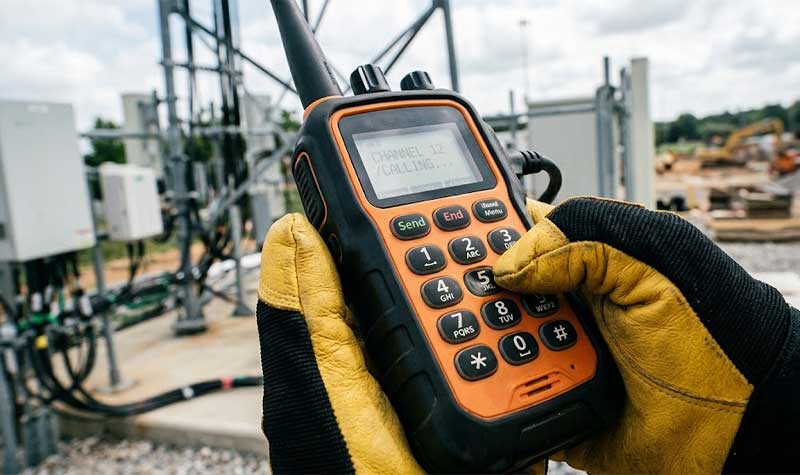 A person wearing heavy duty industrial gloves operates a rugged handheld radio featuring high visibility Telecommunication Devices Silicone Keypads