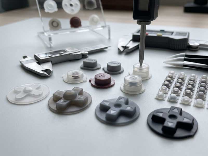 A collection of custom Game Boy Color silicone button sets and directional pads displayed alongside digital calipers and measuring tools