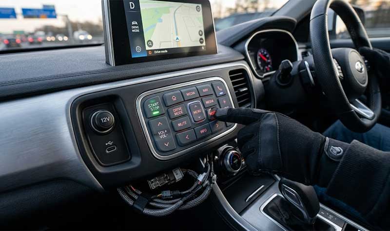 A driver wearing a black glove operates an EMI Shielding Silicone Keypad integrated into a modern cars center console dashboard