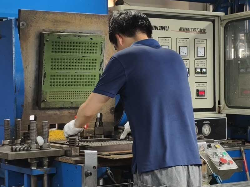 A factory worker operating a compression molding machine to manufacture a silicone keypad mold in an industrial workshop