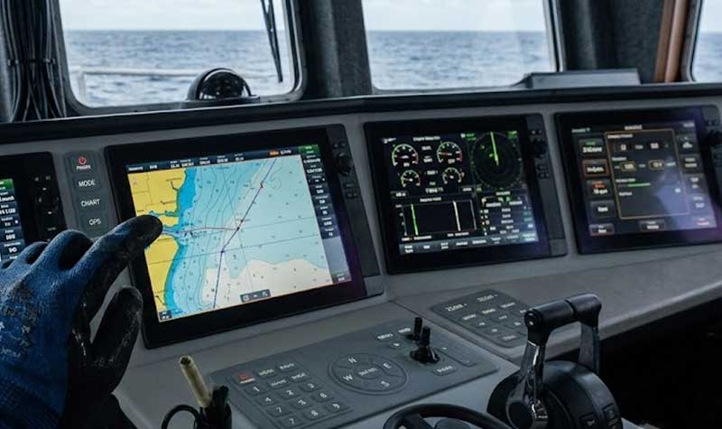 A gloved hand points to a navigation screen on a ships bridge next to a marine console featuring integrated pad printed silicone keypads