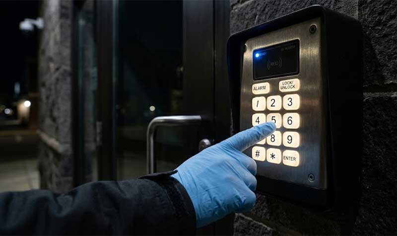 A gloved hand presses a number on an outdoor security keypad at night illuminating each backlit silicone button for clear visibility and access control