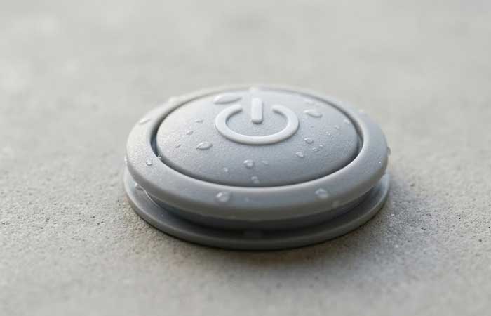 single gray waterproof silicone button featuring a debossed power symbol on its matte surface adorned with small water droplets