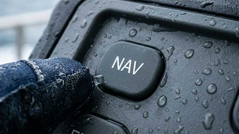 single waterproof silicone button labeled NAV covered in water droplets on a marine control unit being pressed by a gloved hand