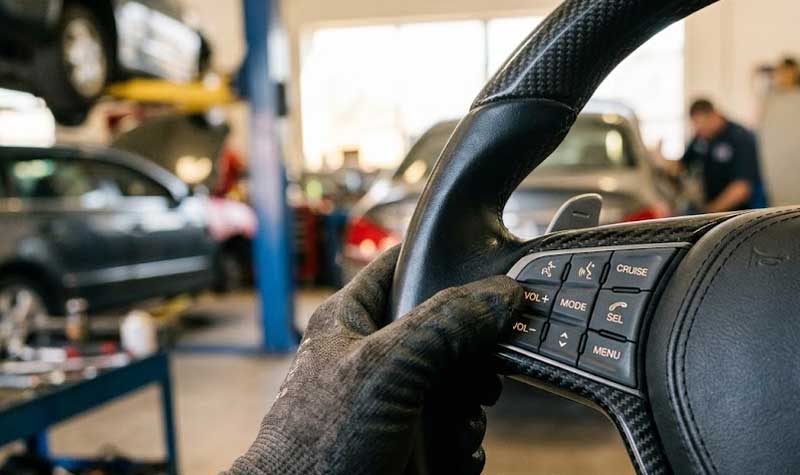 A gloved mechanic tests the wear resistant steering wheel silicone keypads integrated into a carbon fiber steering wheel inside an automotive repair shop