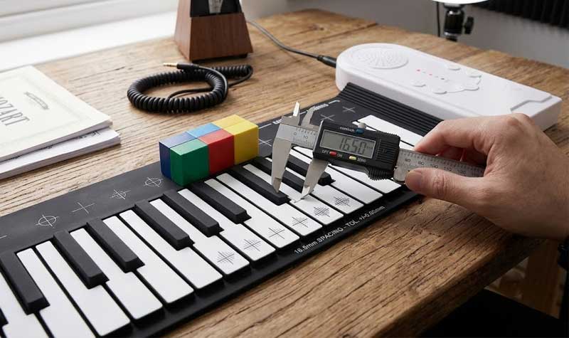A person uses a digital caliper to measure the key spacing on a black and white Silicone Piano Keyboard