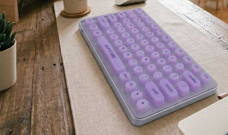 A purple silicone keyboard for long nails with raised cylindrical keycaps on a clean office desk