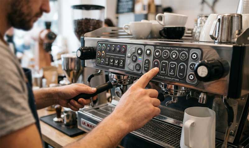 baristas finger interacting with a complex control panel featuring coffee machine silicone keypads with multi function button layouts and custom visual icons