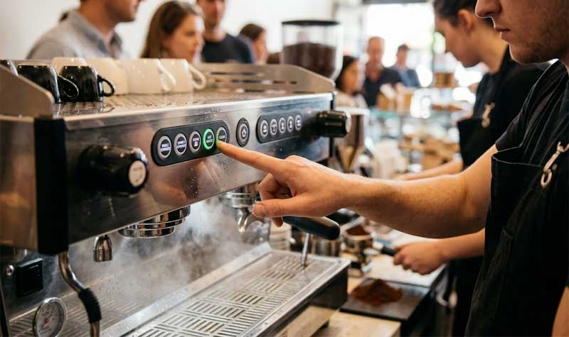baristas finger pressing a button on a coffee machine silicone keypad integrated into a commercial espresso maker in a busy cafe