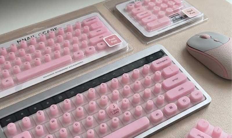 A pink Silicone Keyboard Cover for Long Nails with raised pillar keys sits beside retail packaging on a neat office desk