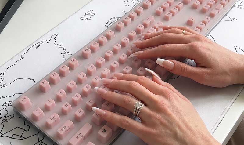 A pink Silicone Keyboard Cover for Long Nails with raised widely spaced keys on a full size keyboard with hands typing at a desk
