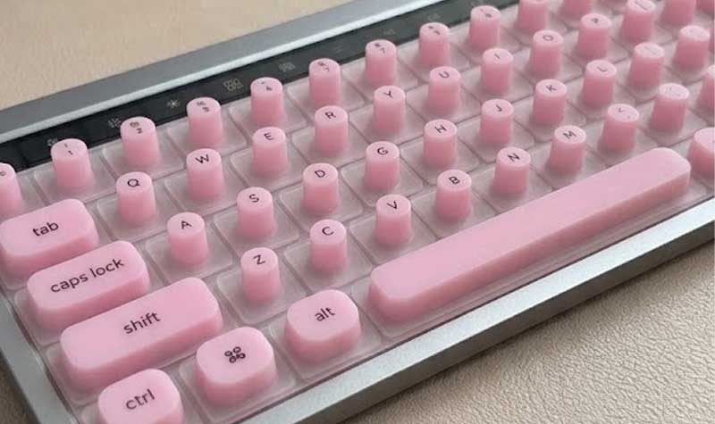 A pink Silicone Keyboard Cover for Long Nails with tall narrow cylindrical key covers sits on a low profile wireless keyboard