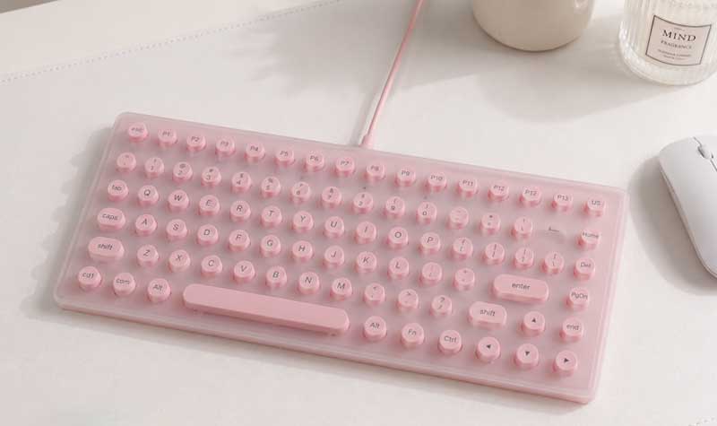 Pink Silicone Keyboard Cover for Long Nails with small raised keys and wide spacing on a compact keyboard beside a white mouse