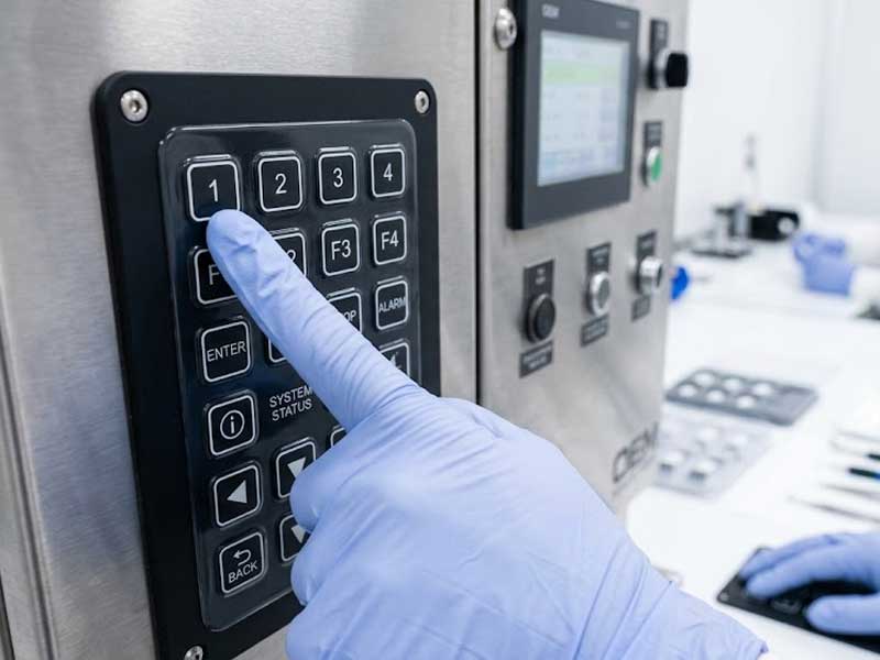 A custom black PU coated silicone keypad mounted on a stainless steel industrial panel with an engineer in the background
