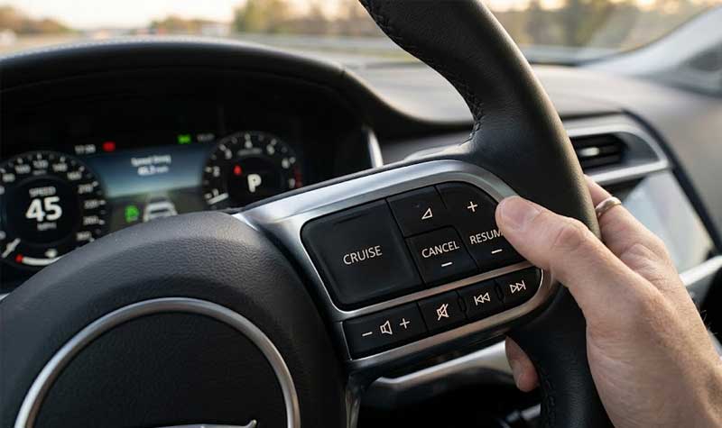 A driver hand operates cruise control and media steering wheel switches featuring integrated tactile silicone buttons inside a car dashboard environment