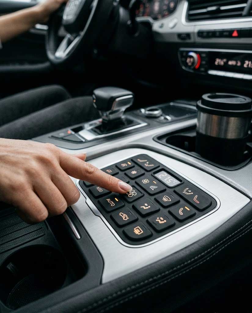 A driver pressing a modern automotive electronics silicone keypad on a vehicle center console interface
