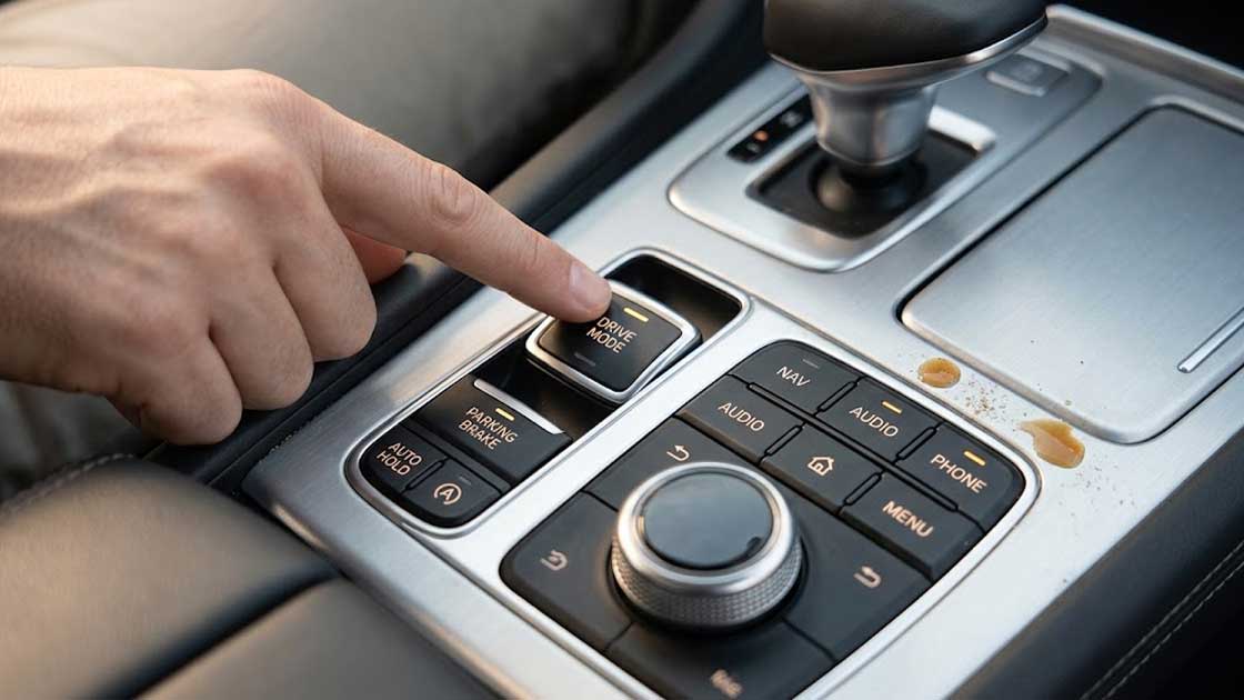 A hand operates durable backlit automotive electronics silicone keypads near a spilled drink on a complex car center console control panel