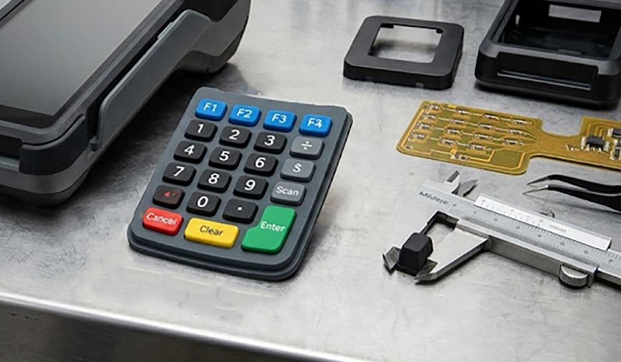 A realistic workstation showing a custom silicone POS keypad alongside a disassembled terminal internal PCB caliper and technical blueprint 1