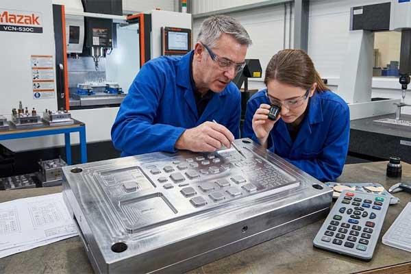 Engineers inspect a metal tooling mold next to a screen printed silicone keypad in a factory workshop